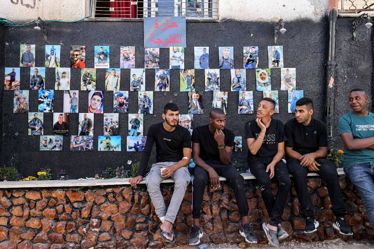 فلسطينيون أمام لوحة تجمع صور شهداء مخيم جنين