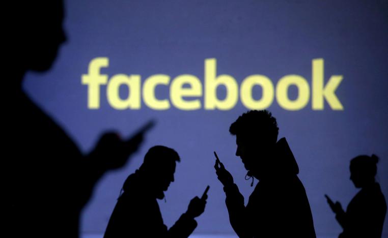 شعار فيسبوك في خلفية مستخدمين يمسكون هواتفهم الذكية