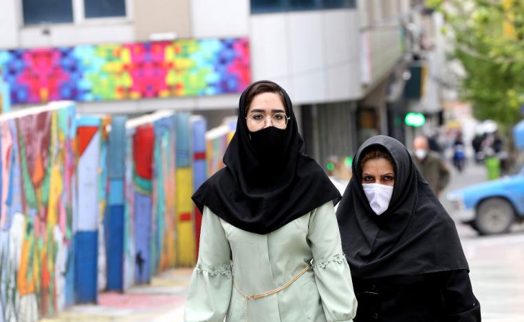 Iranians wearing protective mask walk past graffiti on a wall in Tehran