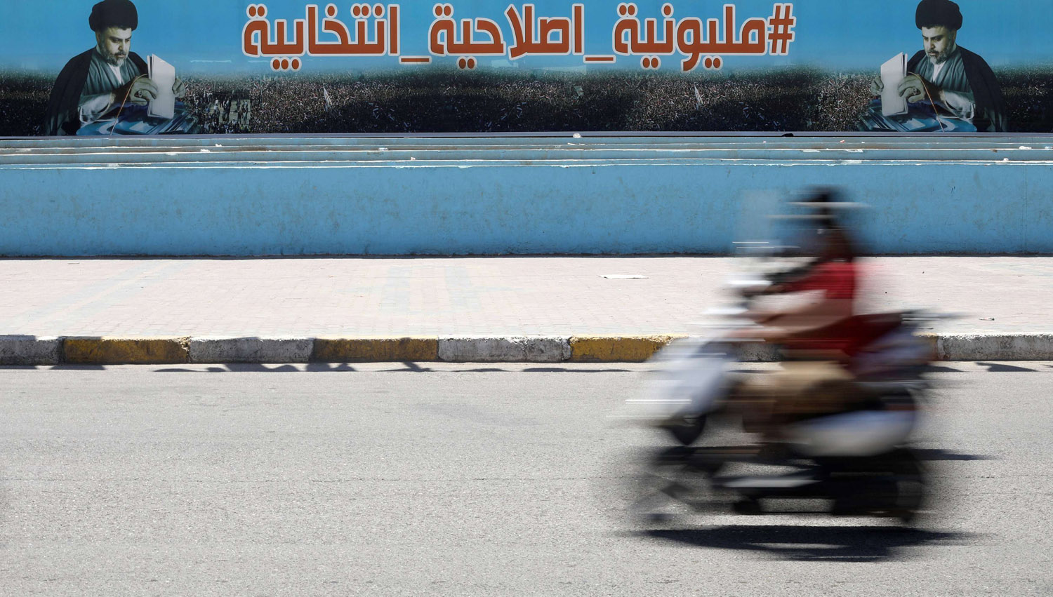 عراقي على دراجة يمر بجانب ملصق انتخابي لكتلة الصدر