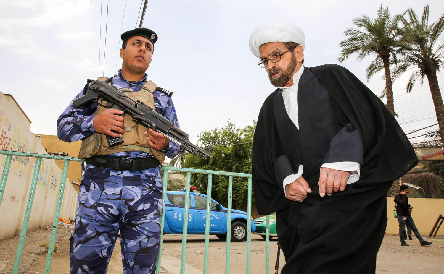 رجل دين شيعي يمر بجانب شرطي عراقي