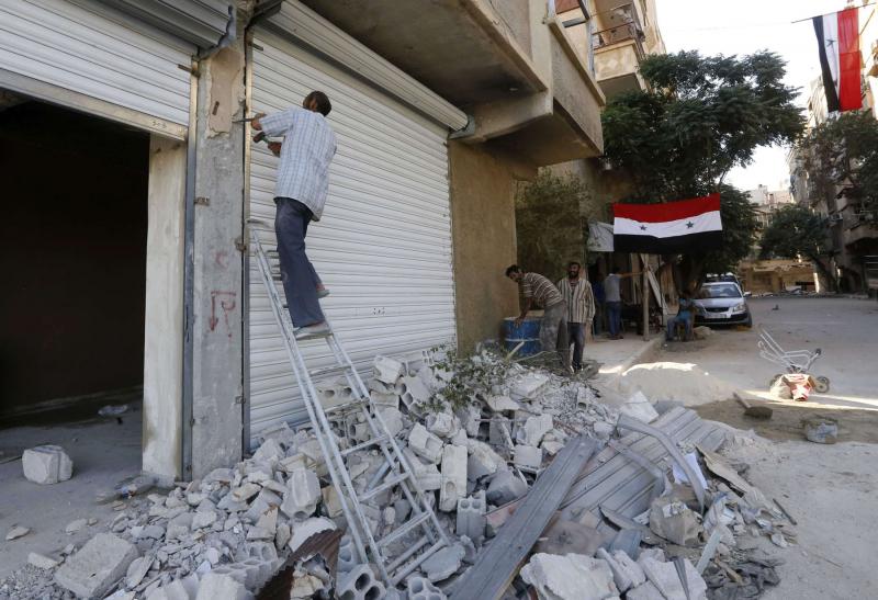 Syrian flags hang from buildings as workers rebuild destroyed stores in Harasta on the outskirt of Damascus, on July 15