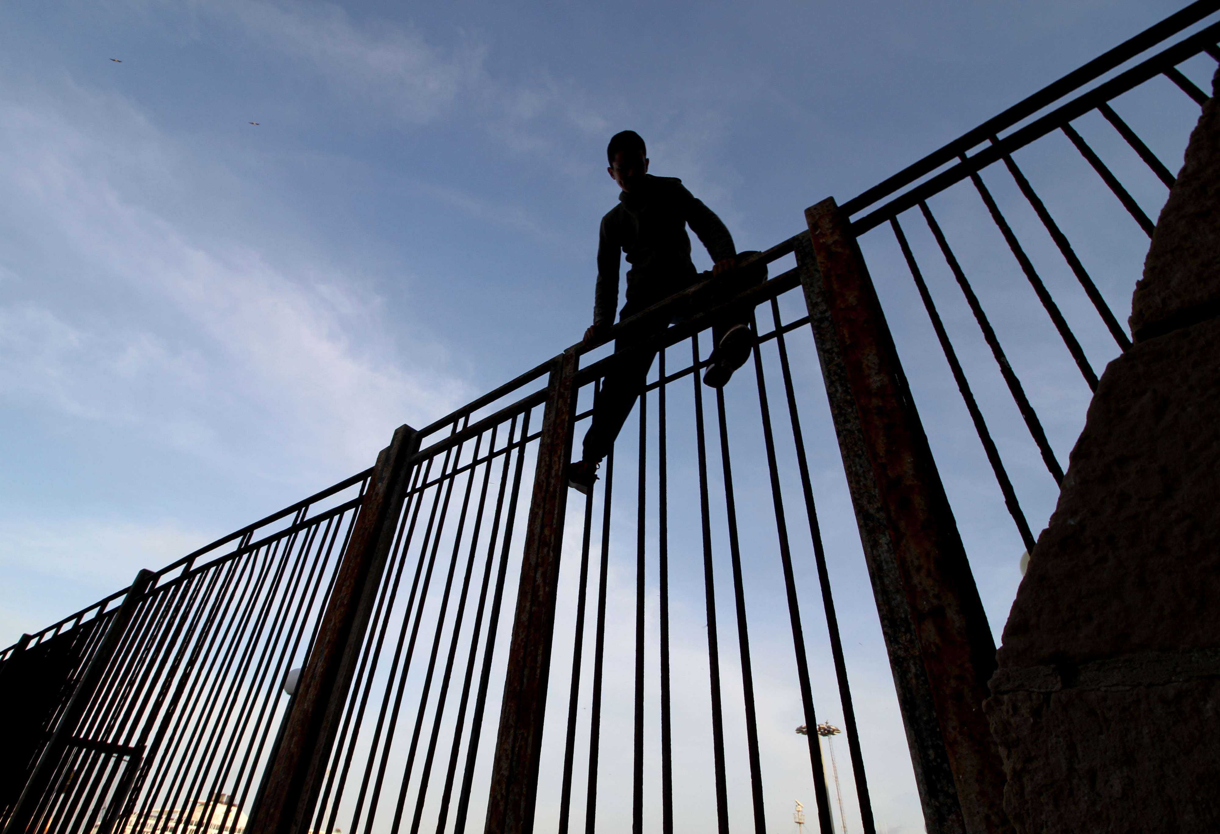 Moroccan youngster climbs a fence in the port of the Spanish enclave of Melilla bordering Morocco