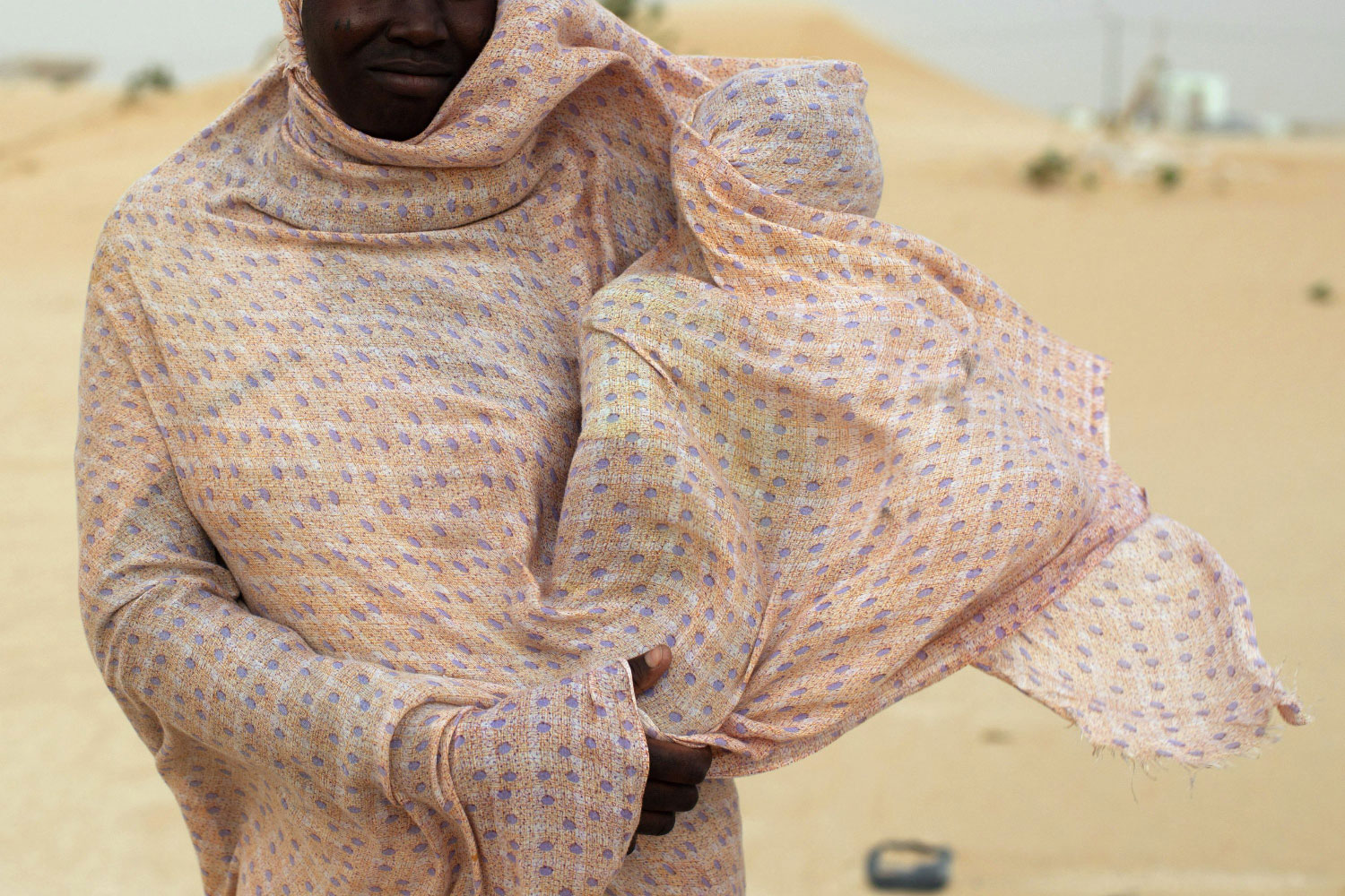 A woman shields her child from the wind while walking on sand dunes near Nouakchott, Mauritania.