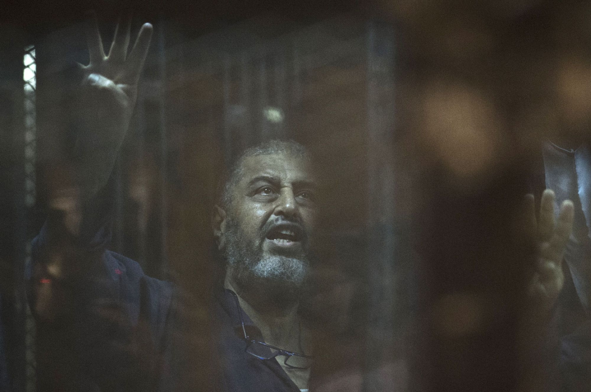 Egyptian Muslim Brotherhood financier Khairat al-Shater gestures from behind the defendant's cage as he attends his trial in Cairo on June 16, 2015. 