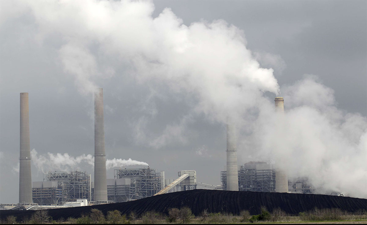 An exhaust rises from smokestacks in front of piles of coal at NRG Energy's W.A. Parish Electric Generating Station in Thompsons, Texas