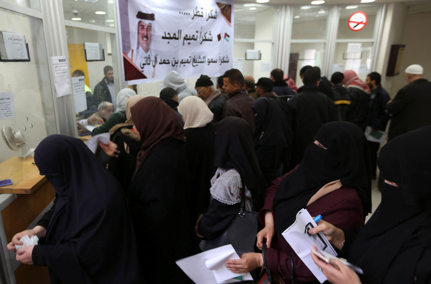 Palestinian Hamas-hired civil servants wait to receive their salaries paid by Qatar as a banner showing a picture of Qatar's Sheikh Tamim bin Hamad Al Thani is seen, in Khan Younis in the southern Gaza Strip December 7, 2018.