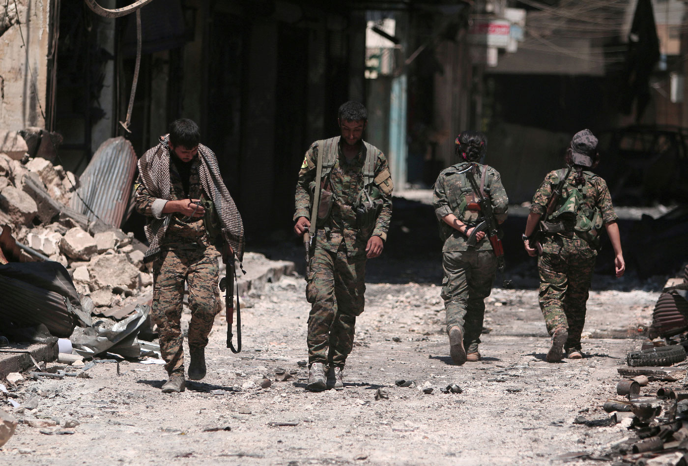Syria Democratic Forces (SDF) fighters walk on the rubble of damaged shops and buildings in the city of Manbij.