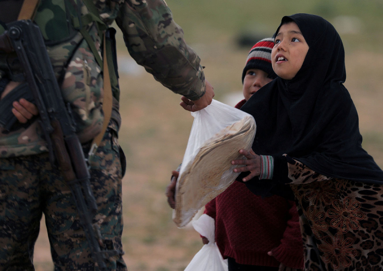 A girl takes a stack of bread from a fighter of Syrian Democratic Forces (SDF) near the village of Baghouz, Deir Al Zor province, Syria February 27, 2019.