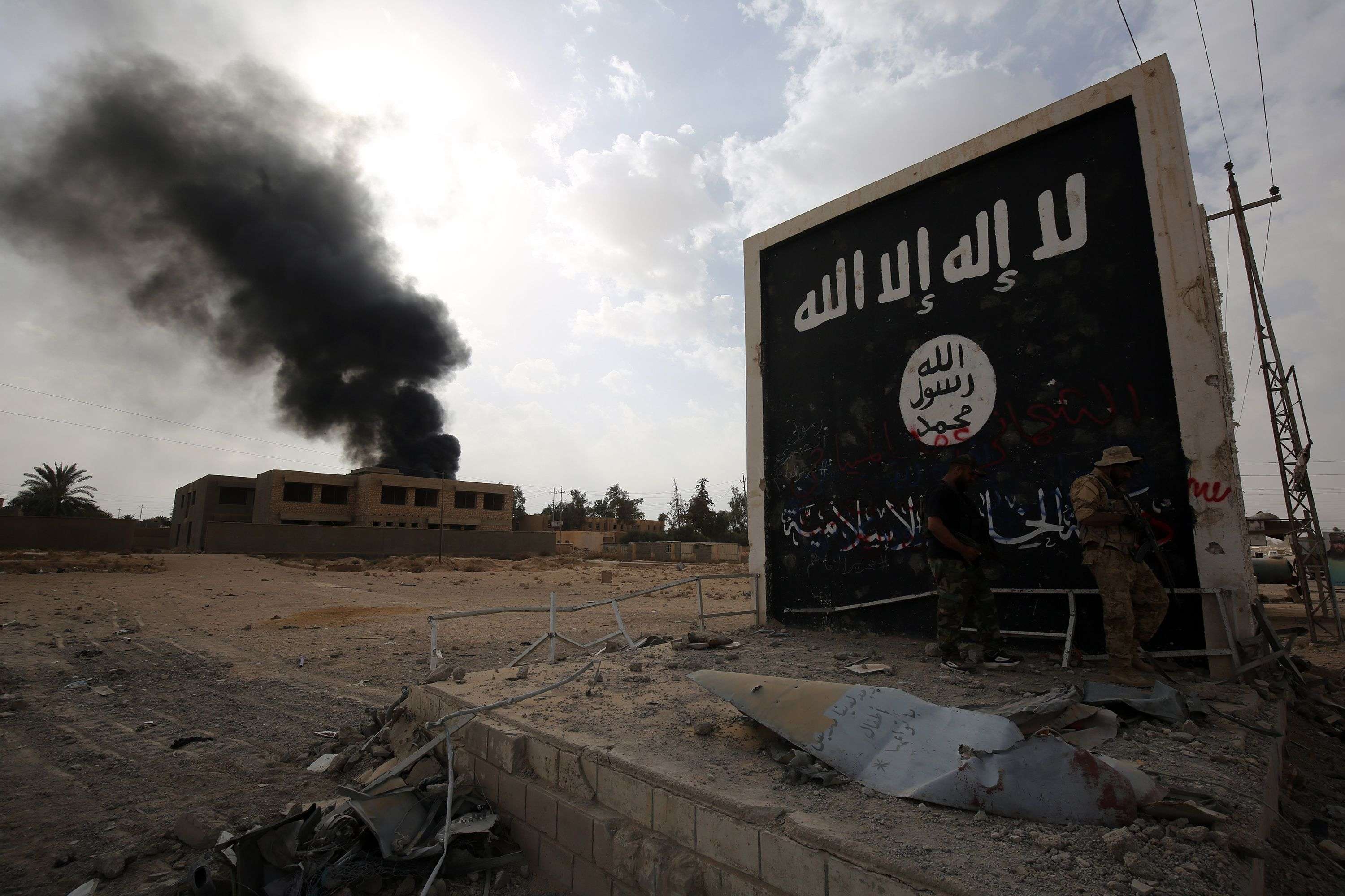 Iraqi fighters of the Hashed al-Shaabi (Popular Mobilisation units) stand next to a wall bearing the Islamic State (IS) group flag as they enter the city of al-Qaim, in Iraq's western Anbar province near the Syrian border as they fight against remnant pockets of Islamic State group jihadists on November 3, 2017.