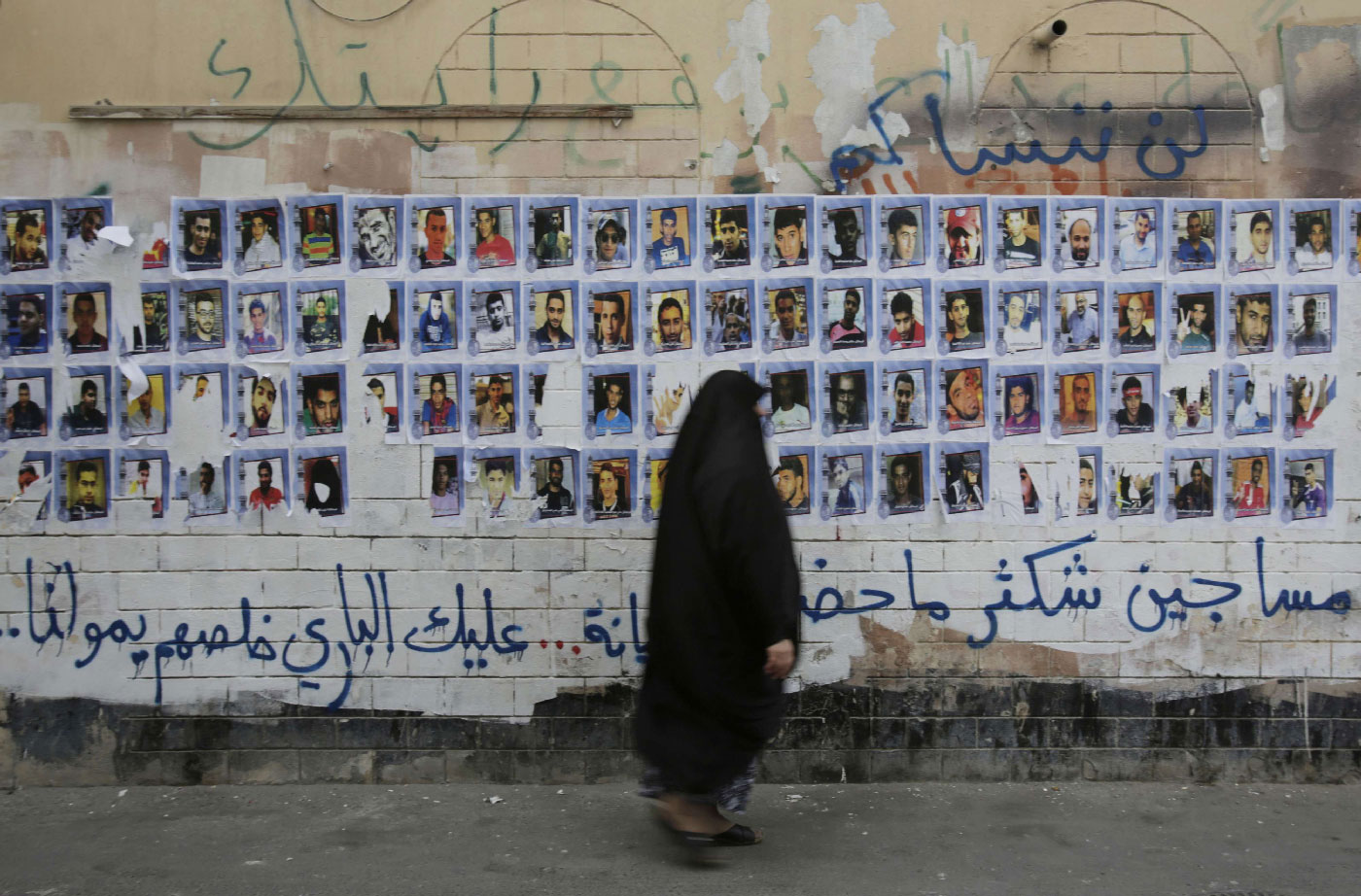 A Bahraini woman walks past images of political prisoners plastered on a wall in Sanabis, Bahrain