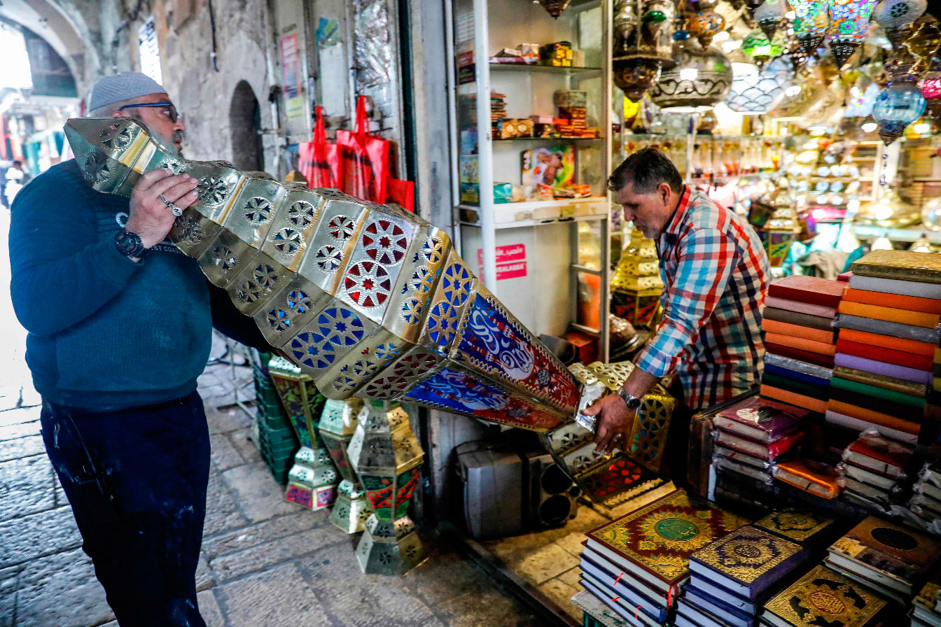 Palestinian craftsman Issam Zughair (R) helps an elderly man transport a large Ramadan lantern