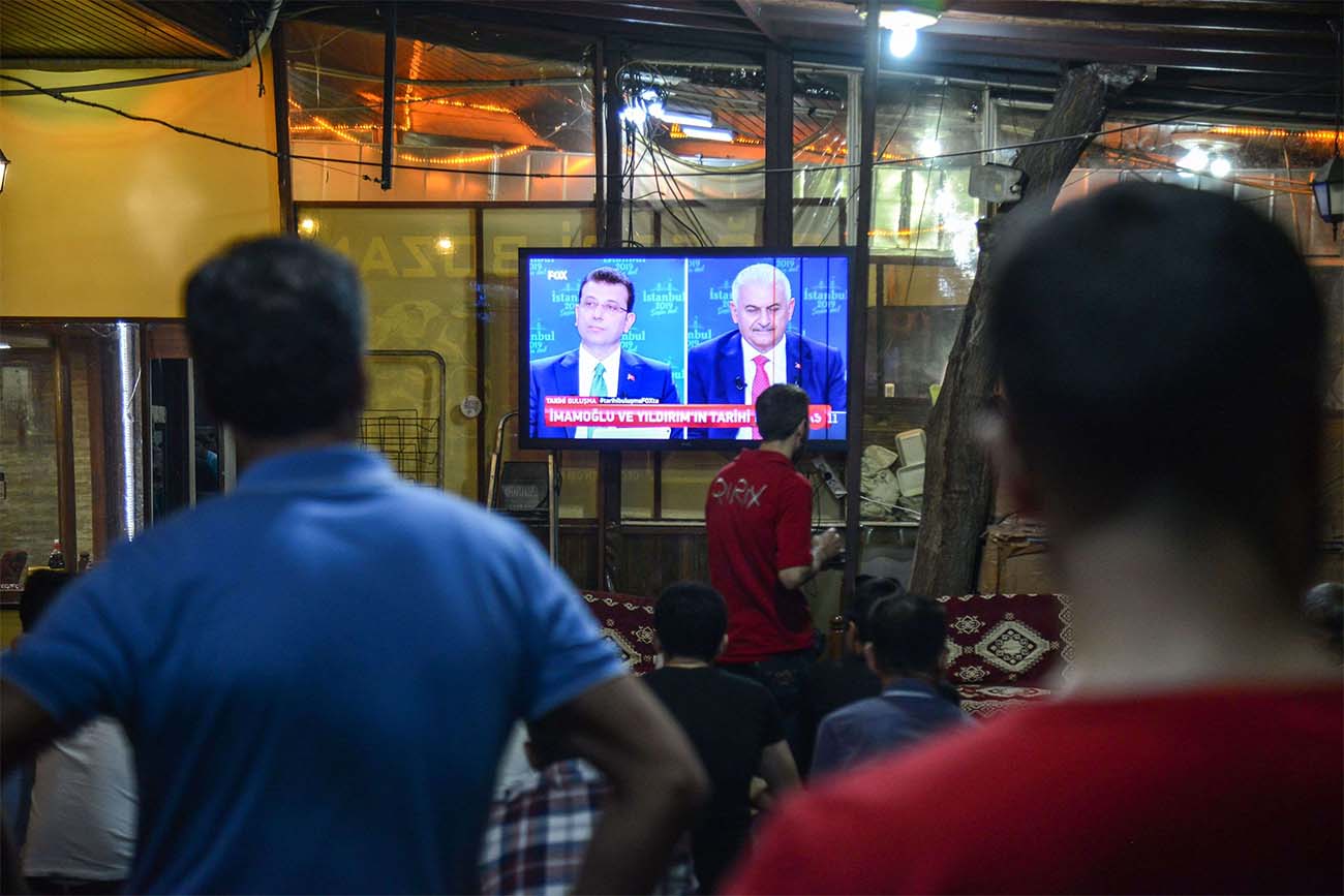 People watch a live broadcast of a televised debate between Istanbul's mayoral candidate Binali Yildirim (R) and Istanbul's deposed mayor Ekrem Imamoglu (L)