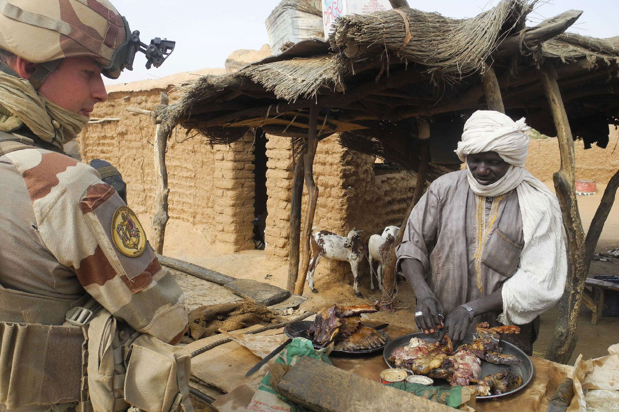 A French soldier speaks with a shopkeeper selling meat at his stall, in Gossi, central Mali