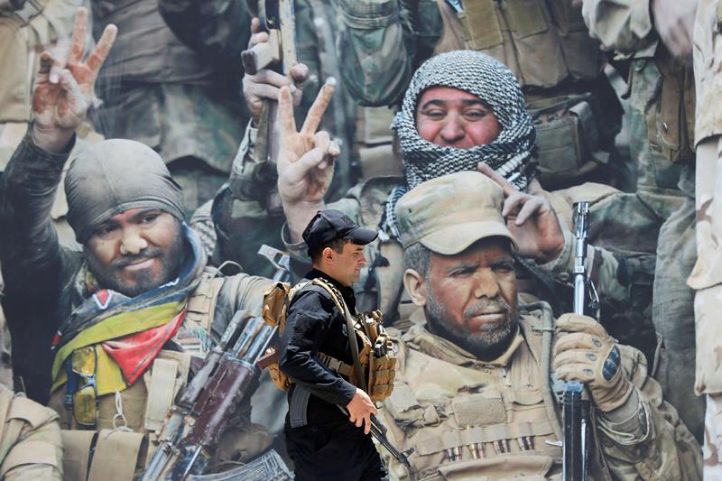 A members of Iraqi Popular Mobilisation Forces (PMF) walks past a poster at the militia group’s media centre in Baghdad, July 2