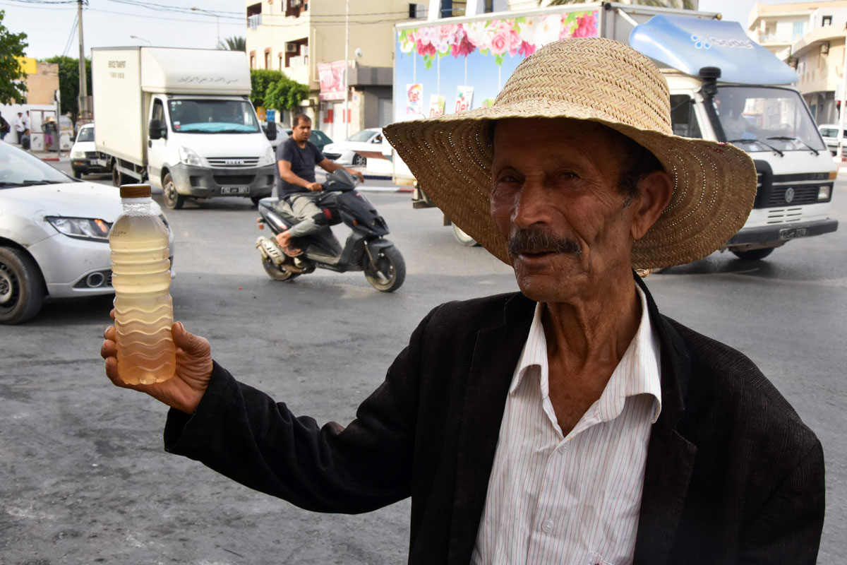 A street vendor holds a bottle of legmi, a coveted date palm drink, in the southwestern Tunisian town of Gabes