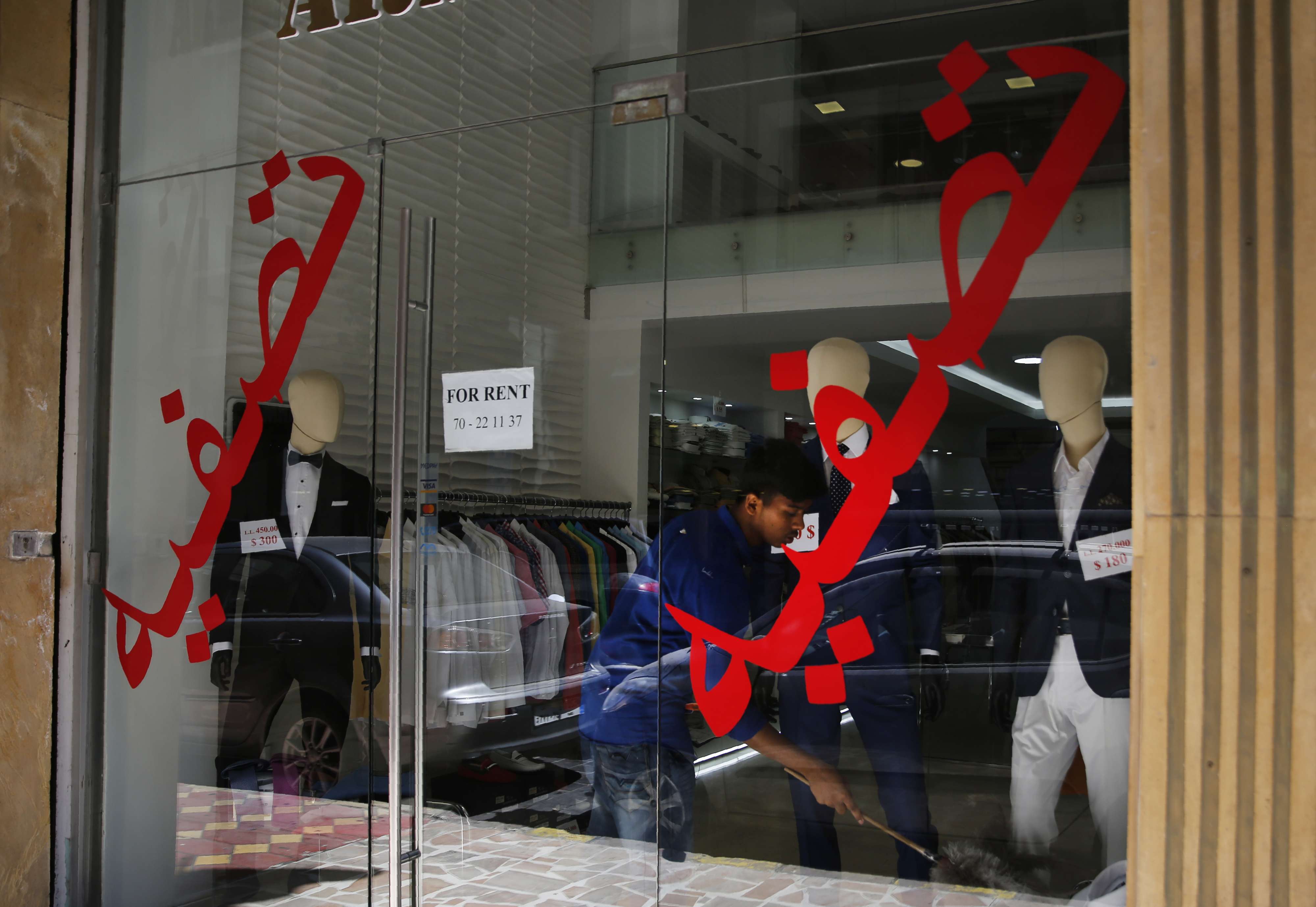 A worker cleans a display in shop with Arabic on the window that reads "liquidation" in Beirut