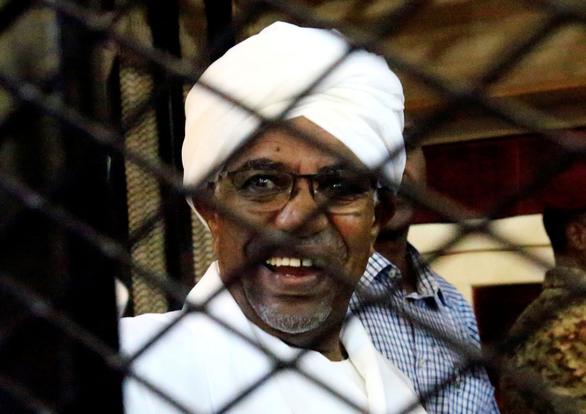 Sudan's former president Omar Hassan al-Bashir smiles as he is seen inside a cage at the courthouse where he is facing corruption charges