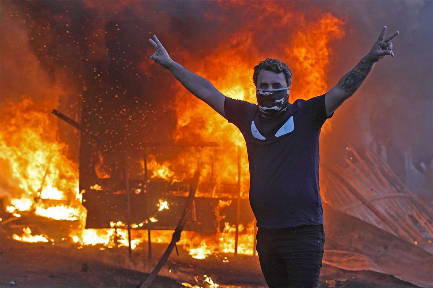 A protester flashes the V for victory sign as a riot police vehicle burns behind him during protests in Baghdad