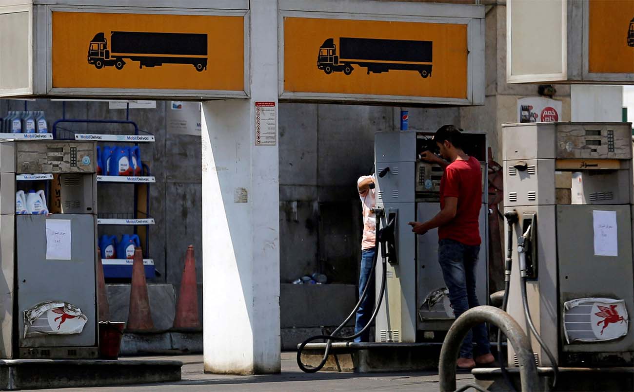 Employees at a petrol station work on a fuel dispenser input a new price of fuel in Cairo
