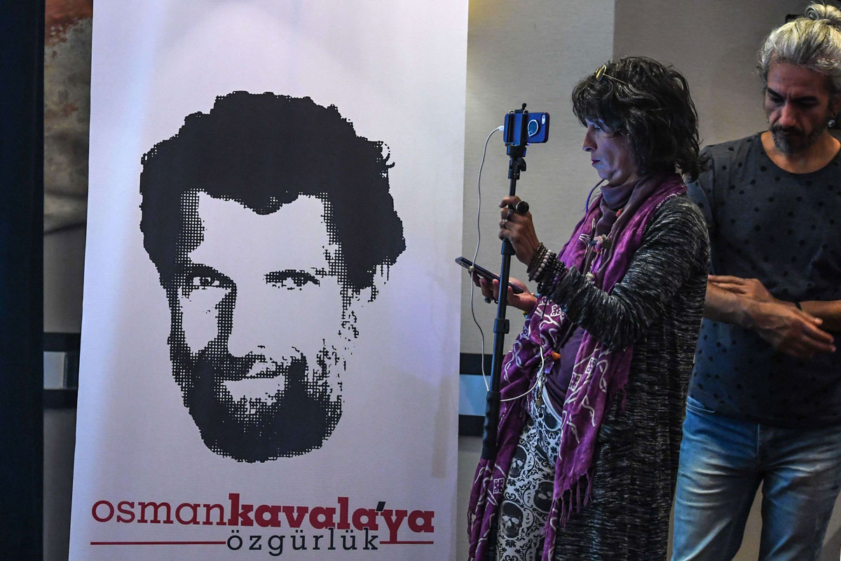 A journalist stands in front of a poster featuring jailed businessman and philanthropist Osman Kavala