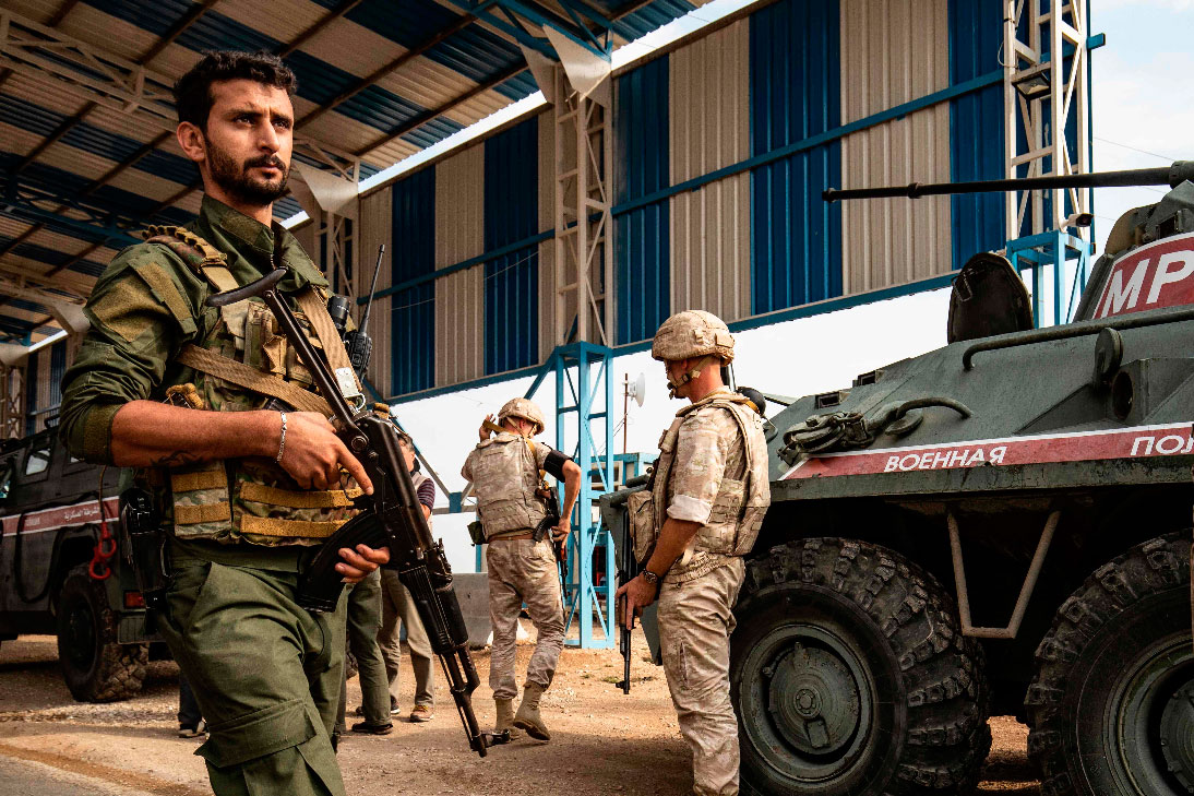 A member (L) of the Syrian Kurdish Asayish internal security forces walks past Russian military police members