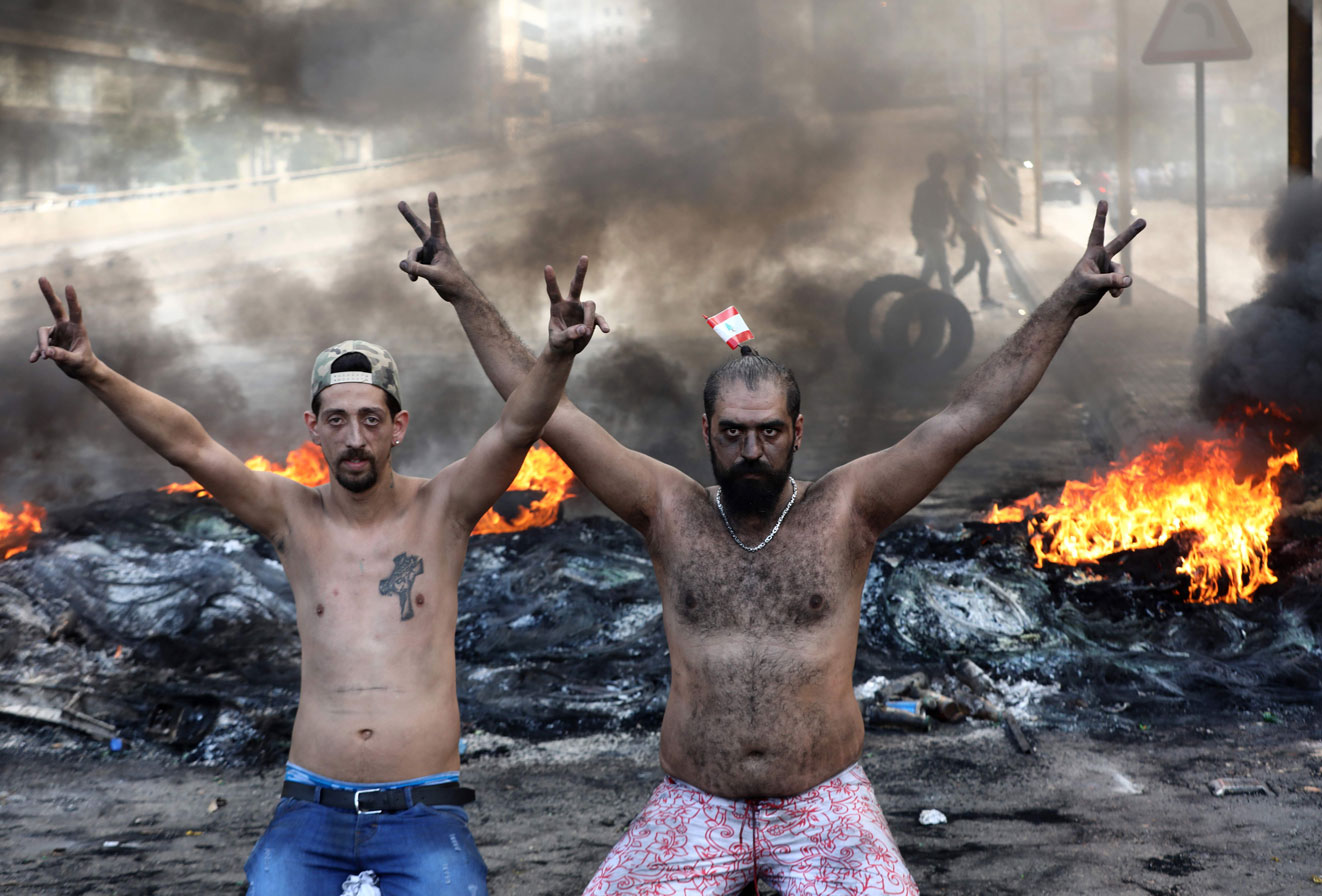 Lebanese demonstrators gesture as tires burn behind them