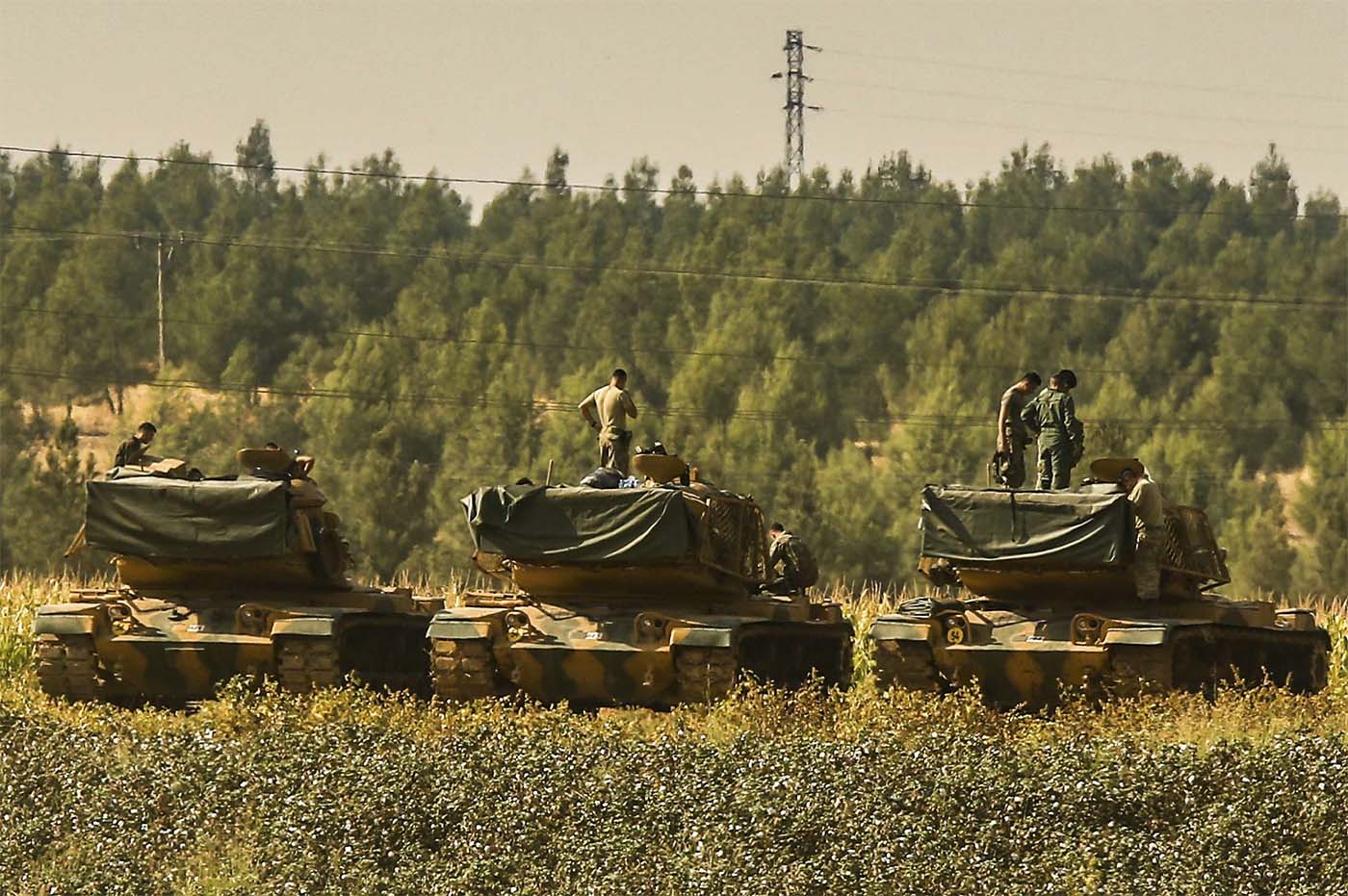 Turkish soldiers stand atop of their tanks at a staging area close to the border with Syria in Sanliurfa province, southeastern Turkey