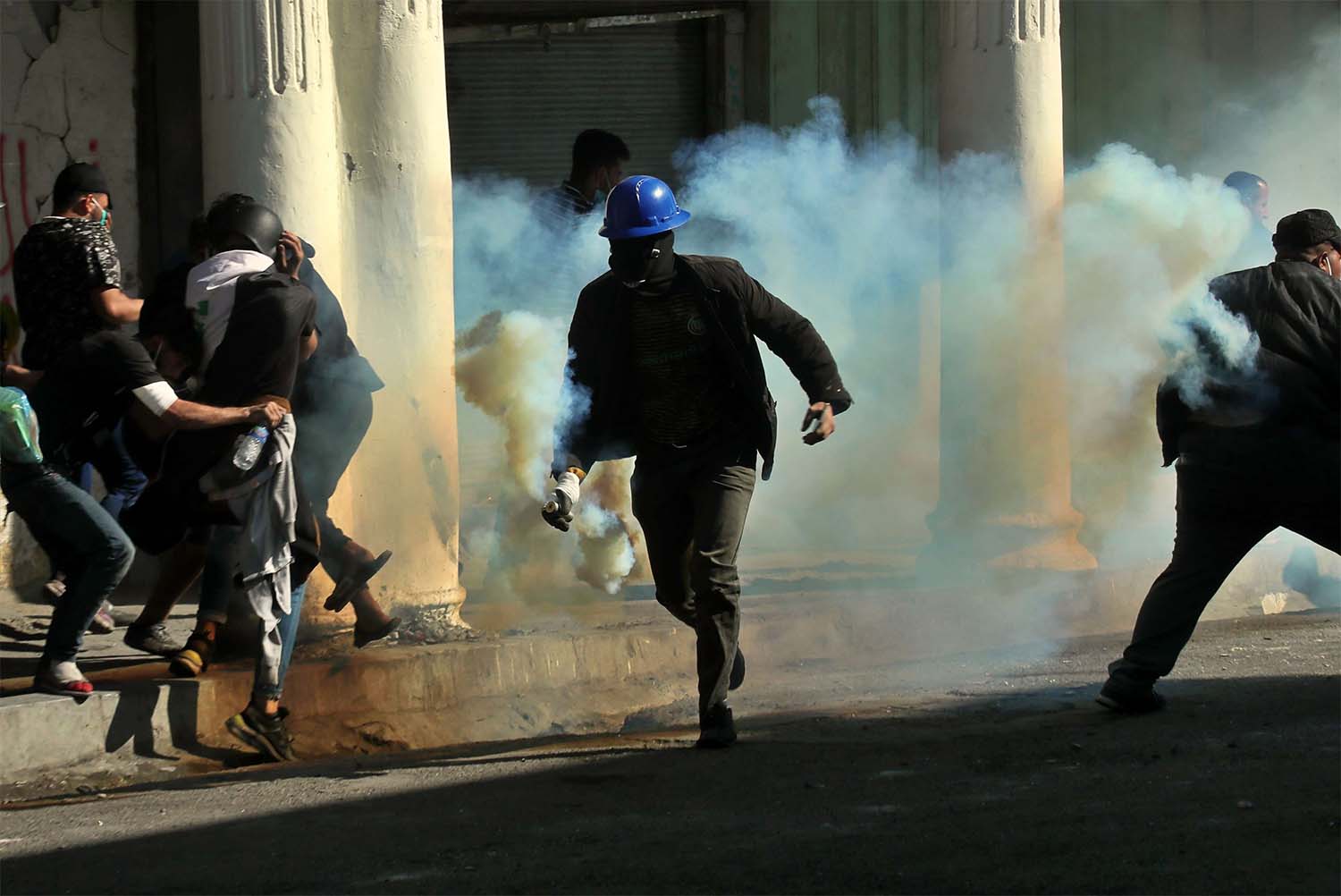 An anti-government protester runs with a tear gas canister fired by police during clashes in Baghdad