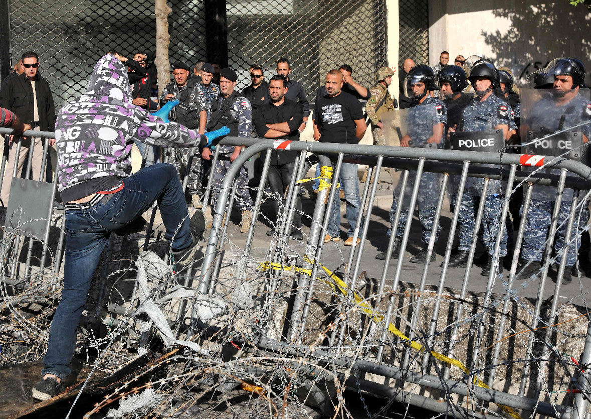 A Lebanese protester steps on a metal barrier through a barbed wire fence near the parliament headquarters in Beirut