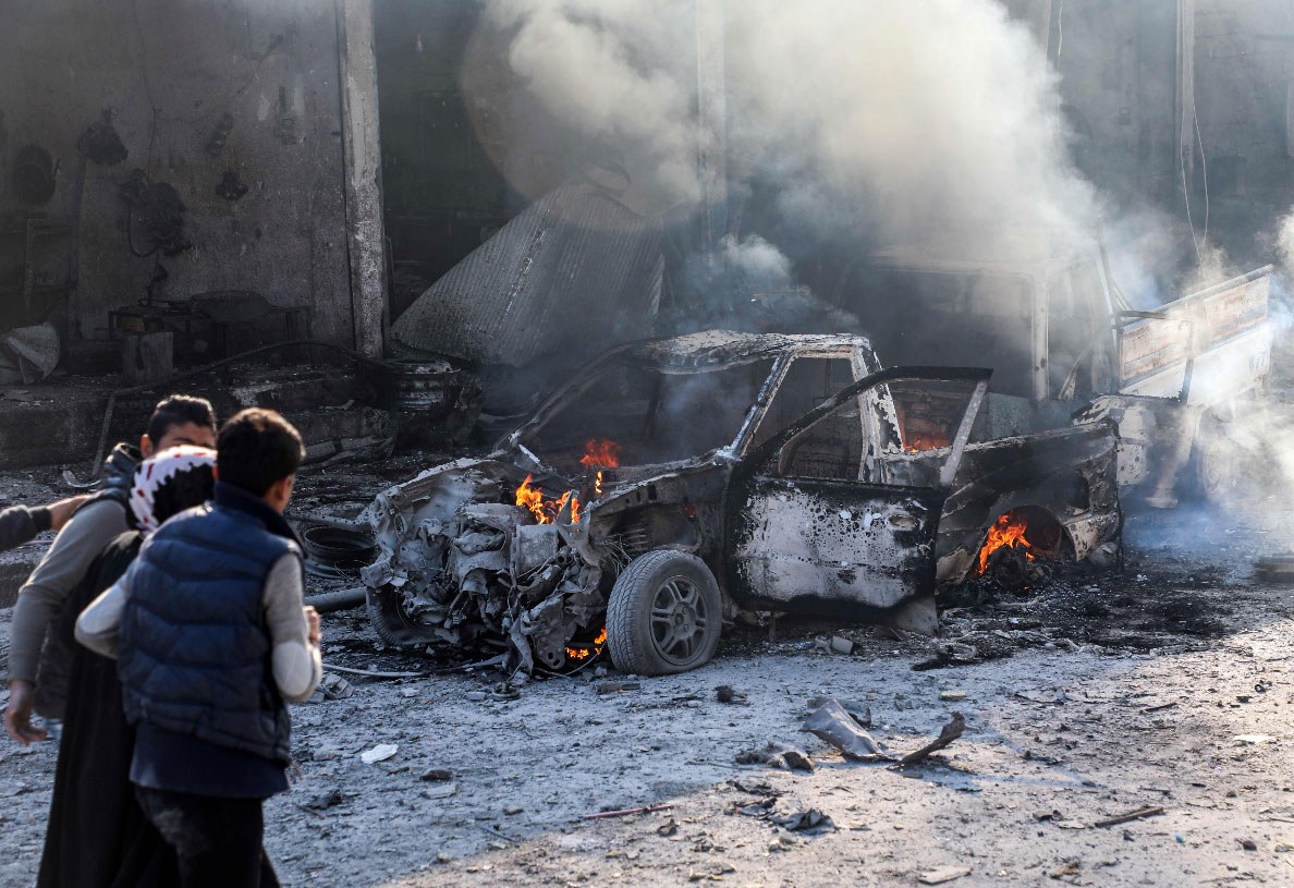 A woman is assisted as she walks past a burning car in Tal Abyad