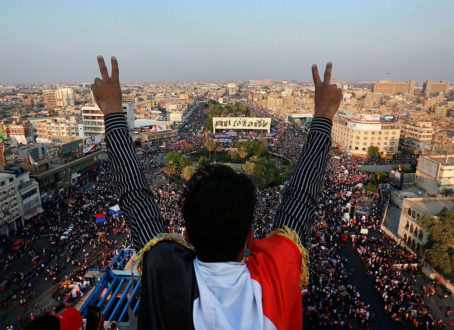 A protester flashes the victory sign while anti-government protesters gather in Tahrir Square during ongoing protests in Baghdad