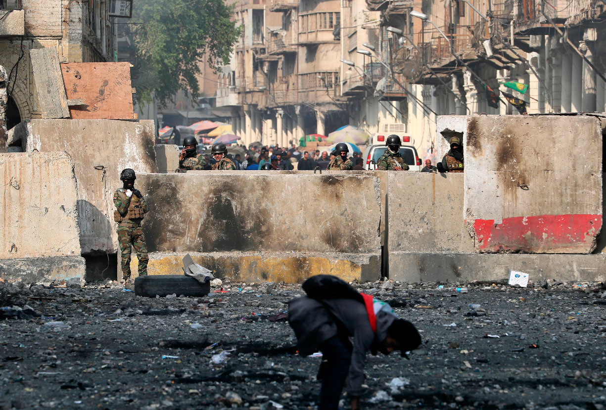 An anti-government protester picks up stones as security forces close Rasheed Street during protests in Baghdad