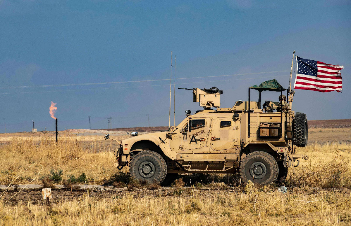 A US armoured vehicle drives past a burning gas flare from oil extraction