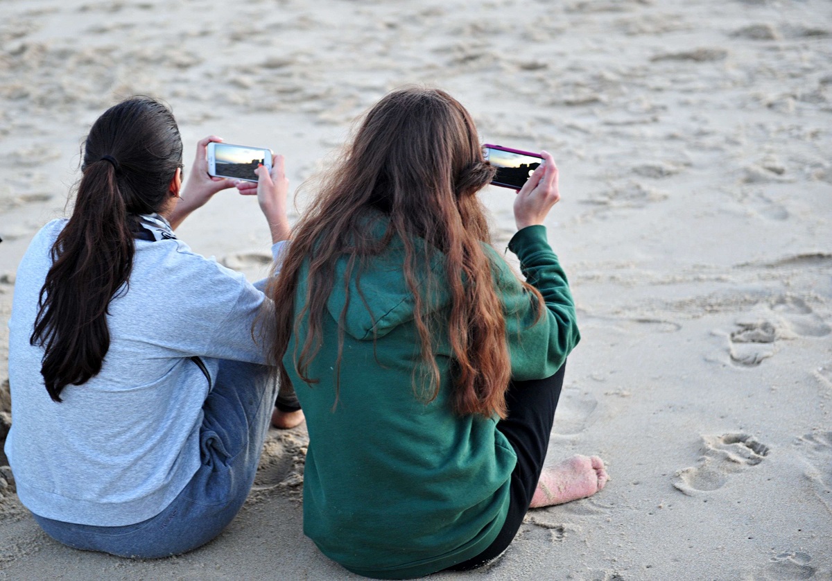 فتاتان تستخدمان هاتفيهما على أحد الشواطئ