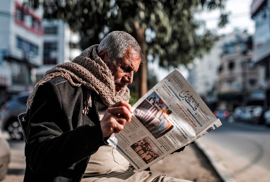 A Palestinian reads the "Filastin" (Palestine) daily newspaper while sitting along a street in Gaza City
