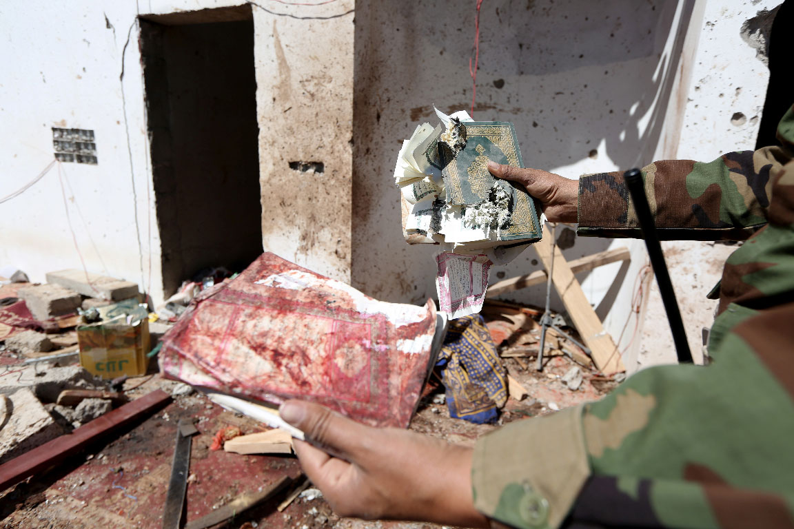 A Yemeni soldier shows a destroyed copy of the Quran at the site of a Huthi missile attack