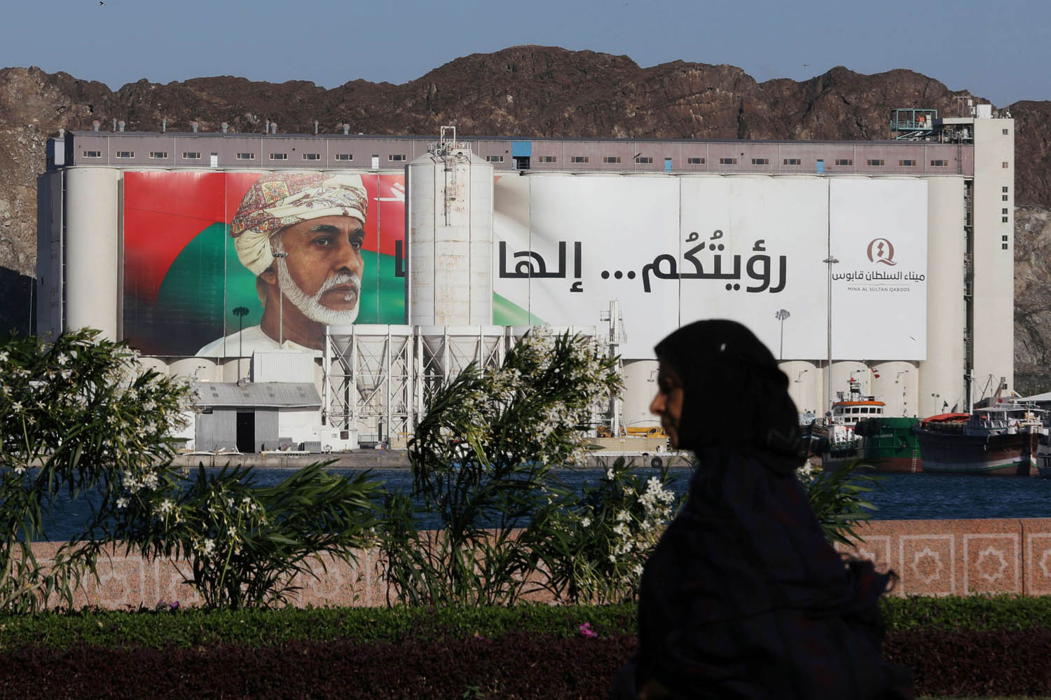 عمانية تمر بالقرب من لوحة تغطي مبنى حكومي في مسقط