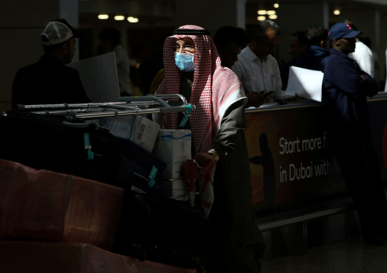 A traveller wears a mask as he pushes a cart with luggage at Dubai International Airport