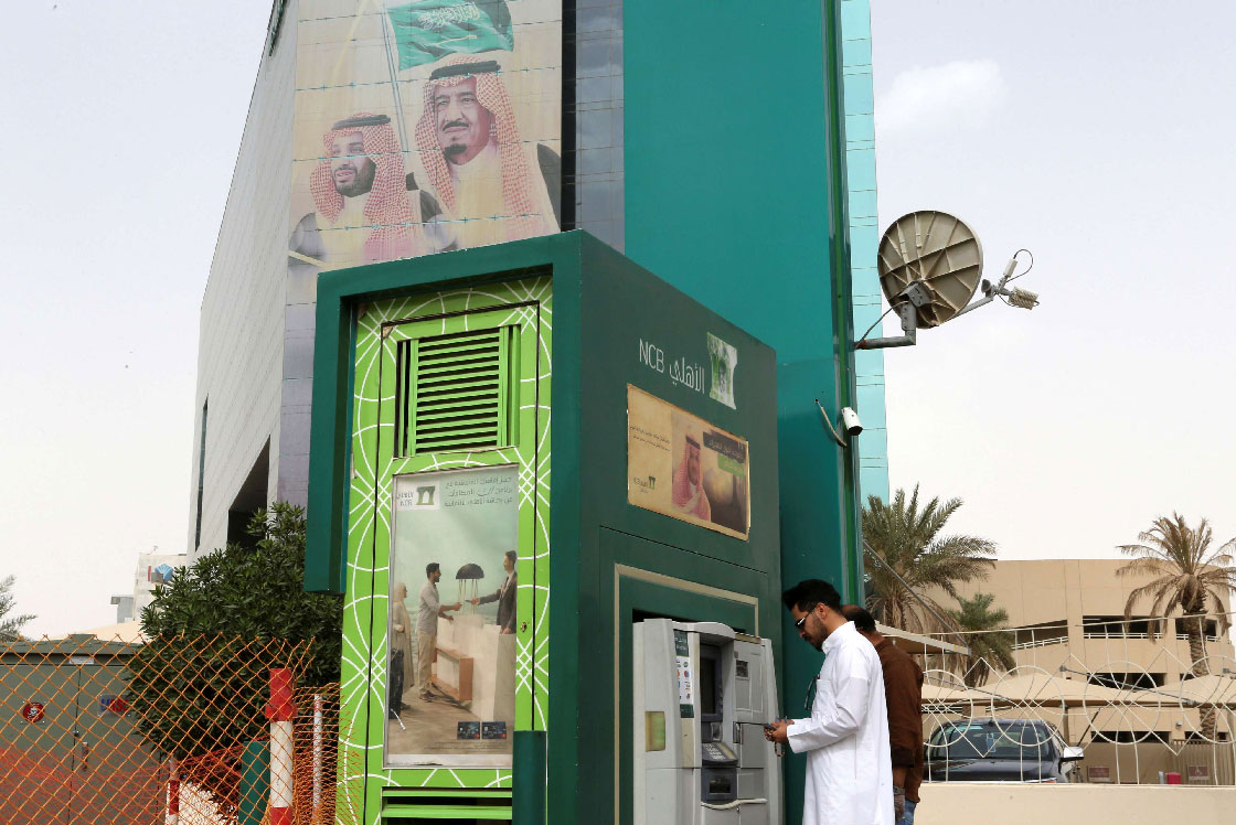A man withdraws money from an ATM outside the Saudi National Commercial Bank