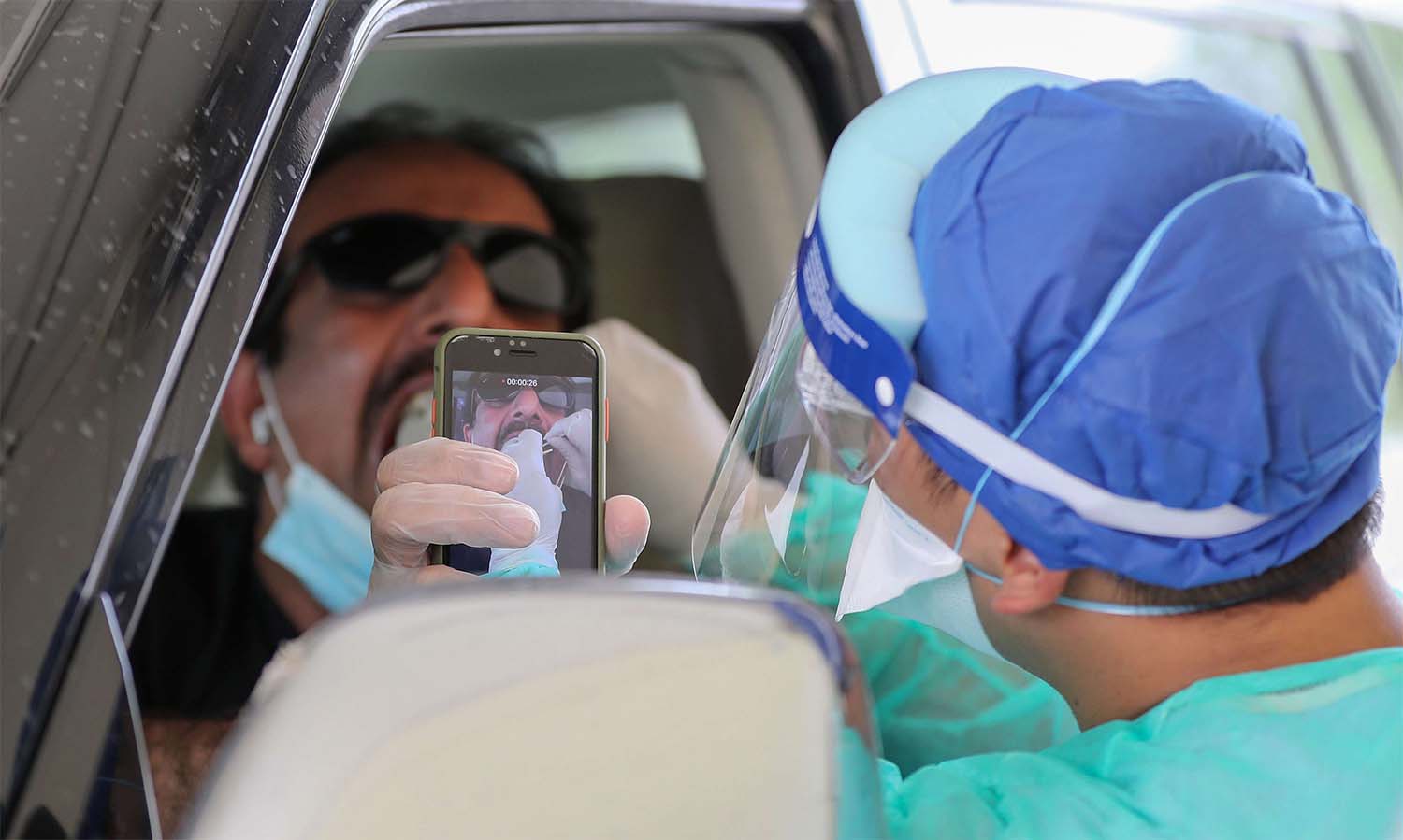 A health worker collects a swab sample from a man at a drive-thru testing service for COVID-19 coronavirus in Doha