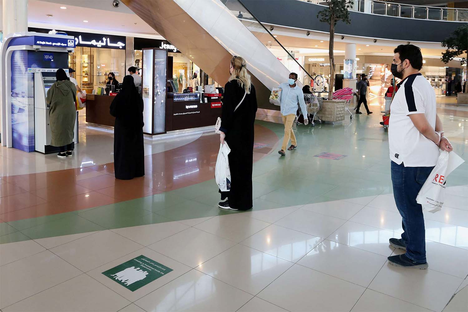 People line up while practicing social distancing to use an ATM at a shopping mall 