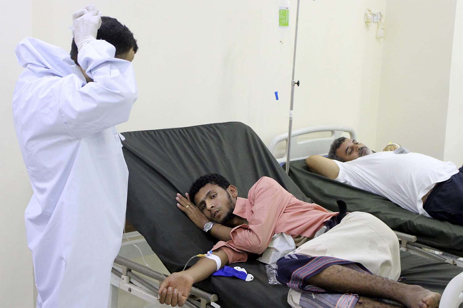 Yemeni doctor talks to a patient receiving treatment and lying on a bed at a hospital in Aden