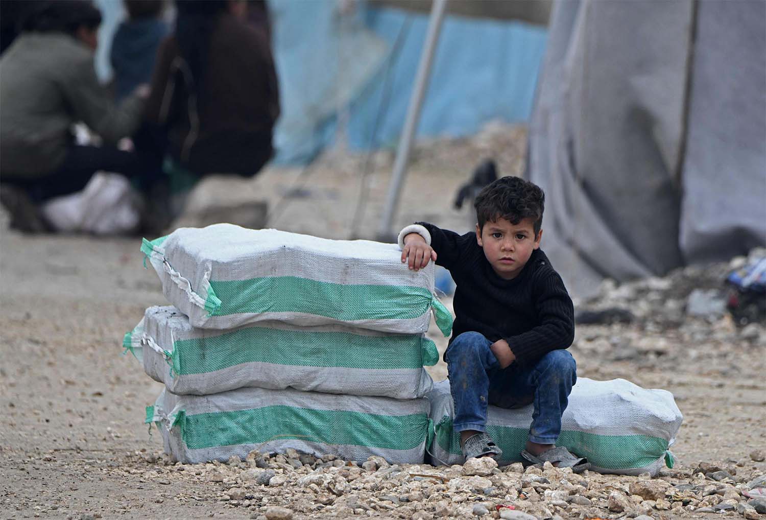 Displaced Syrian boy sits next to humanitarian aid