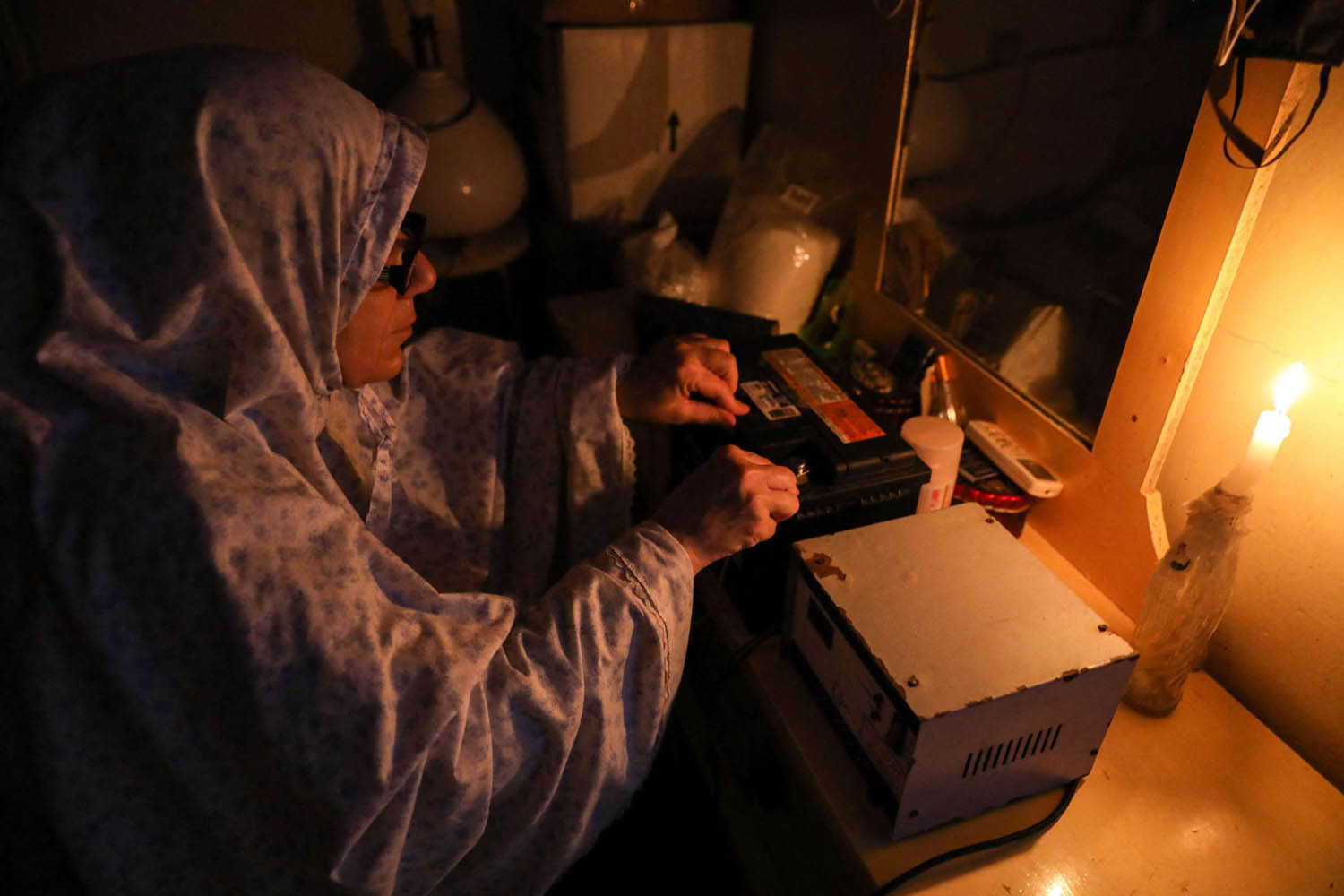 سيدة لبنانية تحاول تشغيل جهاز على بطارية سيارة على ضوء الشموع