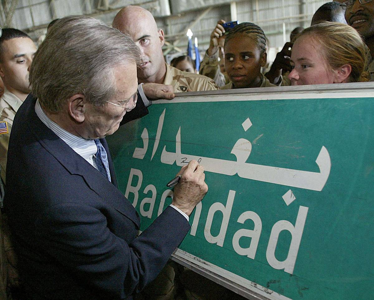 وزير الدفاع الأميركي دونالد رمسفيلد يوقع على لافتة شارع تشير إلى اسم بغداد بعد احتلالها (2003)