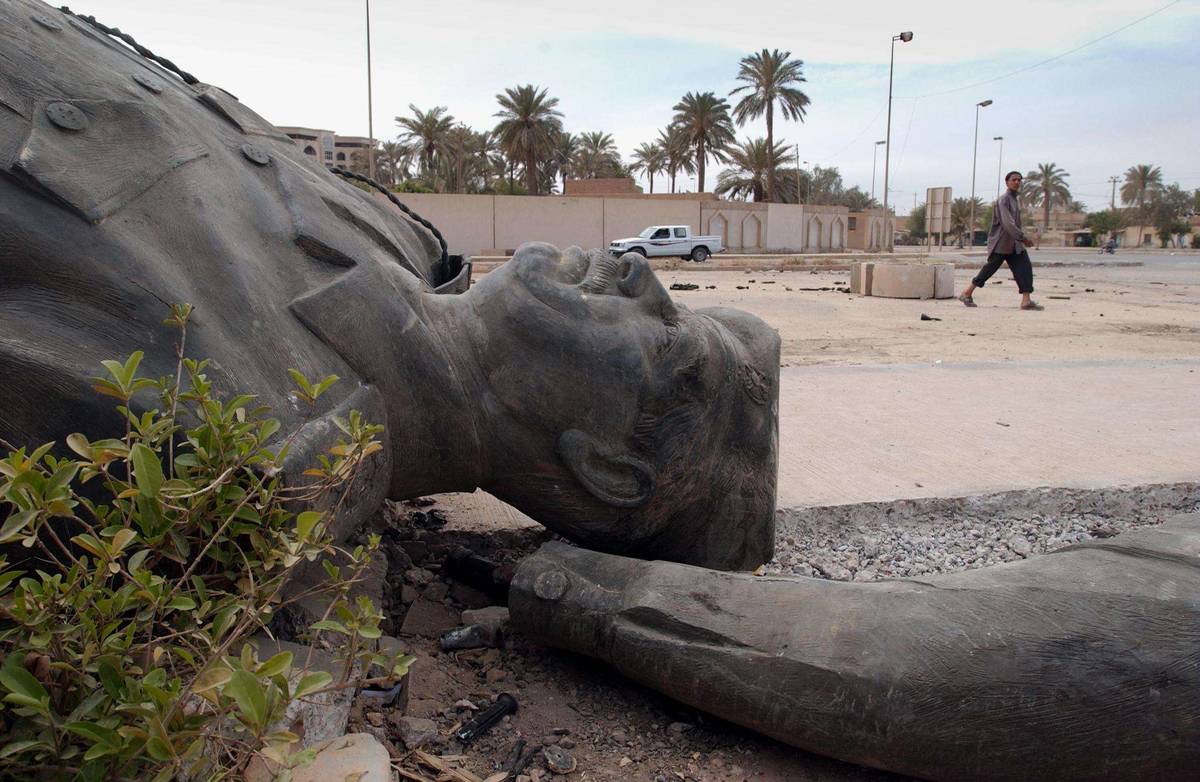 عراقي يمر بتمثال مهشم للرئيس العراقي صدام حسين وسط بغداد (2003)