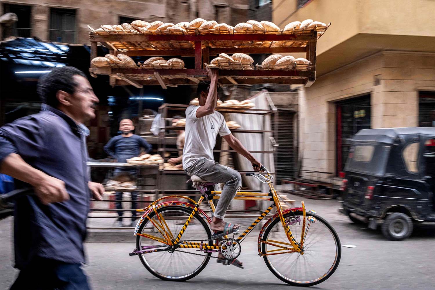 A deliveryman balances a tray of freshly baked bread while riding his bicycl