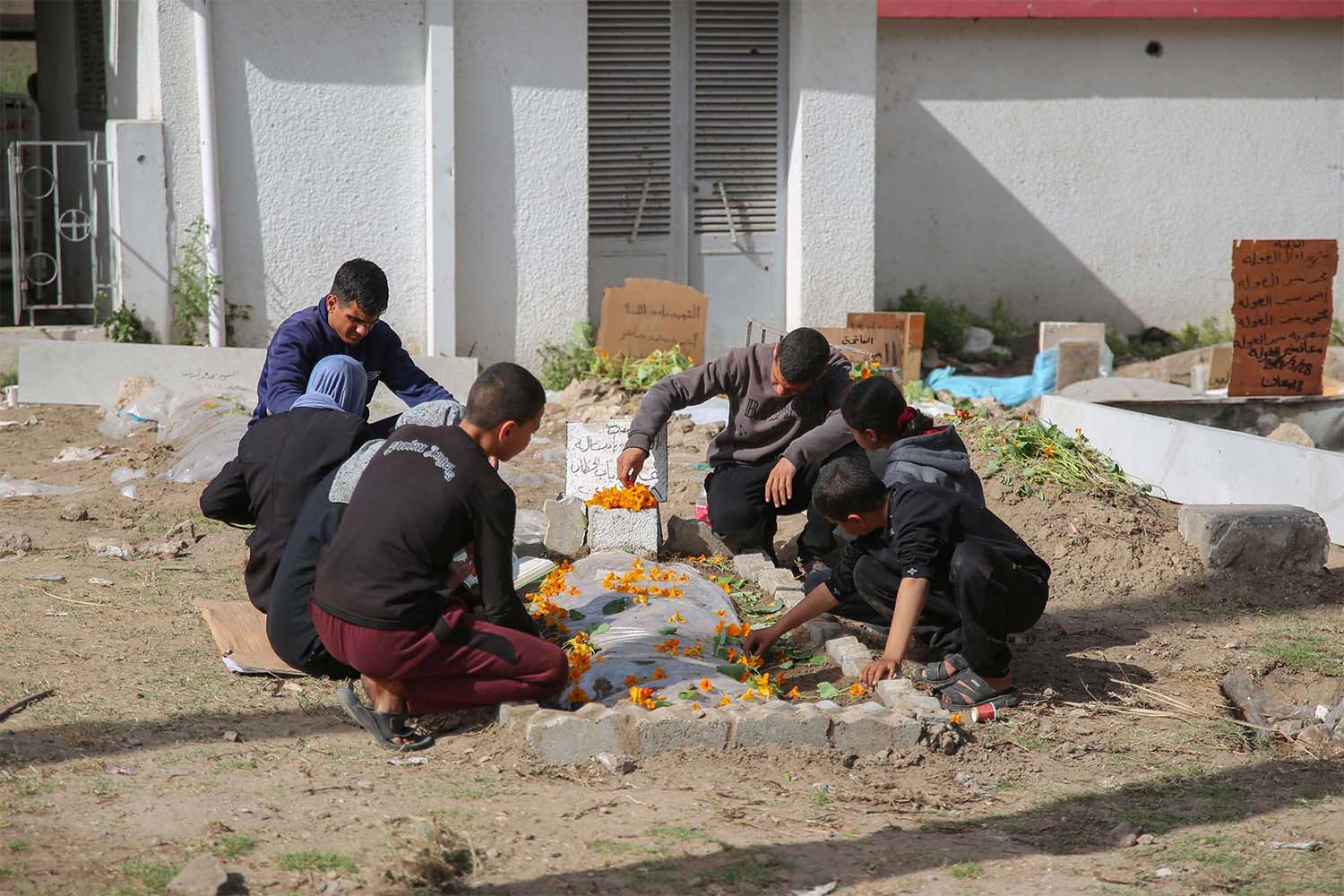 Palestinian mourners gather around a fresh grave at the grounds of the Baptist Hospital