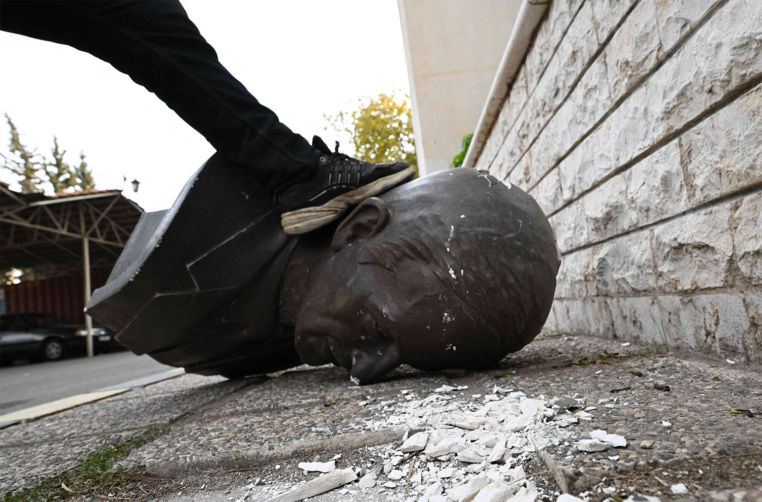 An anti-government fighter steps on the head of a broken statue of late Syrian president Hafez al-Assad